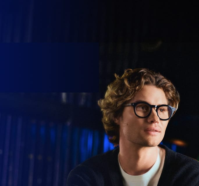 Chase Stokes wears black square Zenni frames in a moody lounge setting.