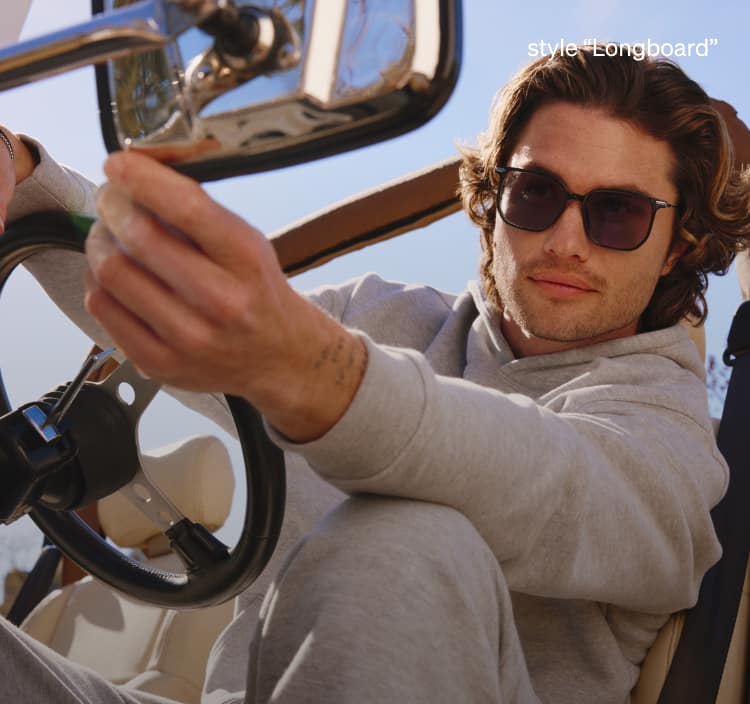 Chase Stokes sitting in a jeep outdoors against a blue sky, wearing “Longboard” full rim square sunglasses from Zenni.