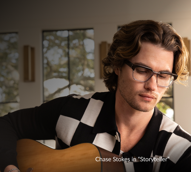 Chase Stokes wearing Zenni rectangle glasses, playing guitar in a checkered shirt.