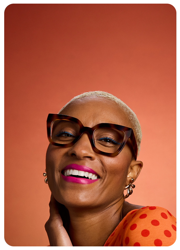 A woman in bold Zenni tortoiseshell square glasses smiles confidently in an orange polka dot top.