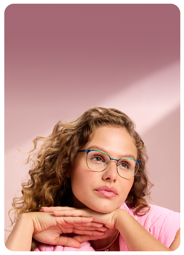 Woman in pastel pink jacket resting her chin on her hands, wearing Zenni teal glasses.