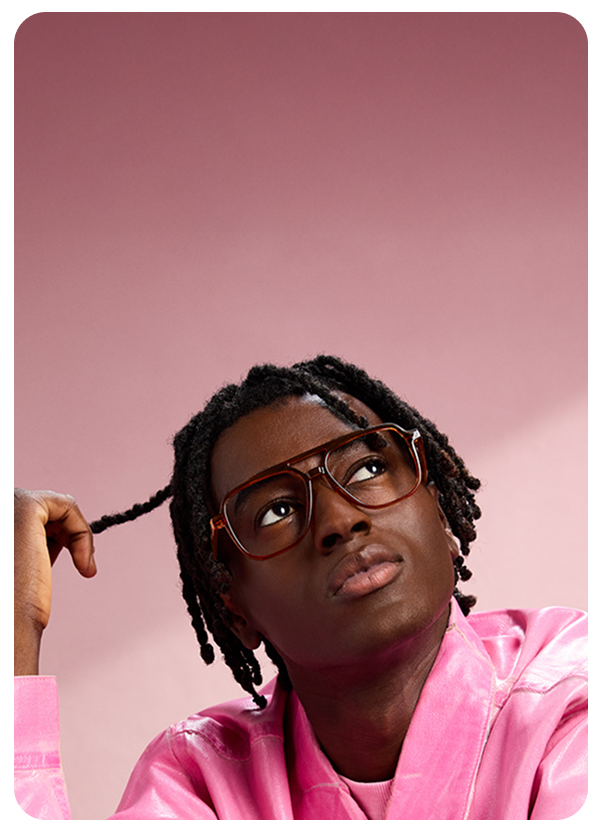 Man in pink jacket looking up while wearing Zenni oversized brown square glasses, pink background.