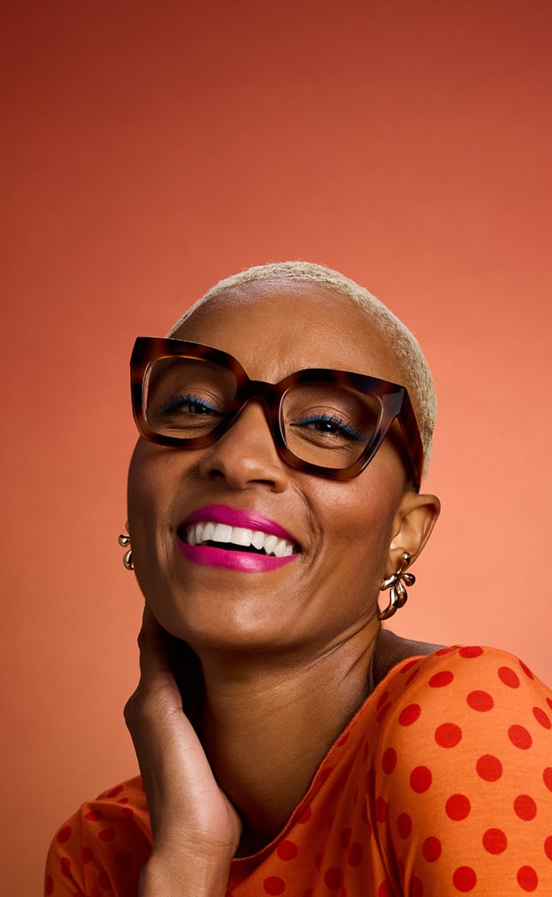 A woman in bold Zenni tortoiseshell square glasses smiles confidently in an orange polka dot top.