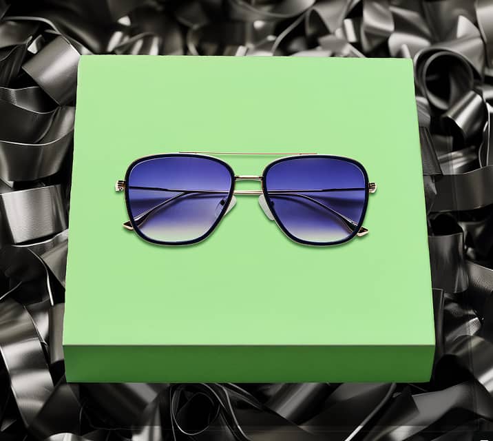 Aviator-style sunglasses with blue tinted lenses displayed on a green box against a black metallic background.