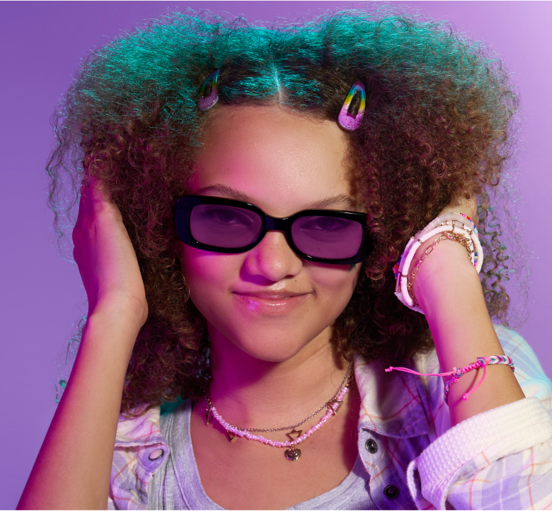 A teen girl with reddish brown curly hair wearing rectangle glasses with purple Blokz+ Tints lenses.