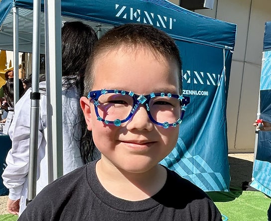 A child standing in front of the Zenni event booth wearing bedazzled Zenni glasses.