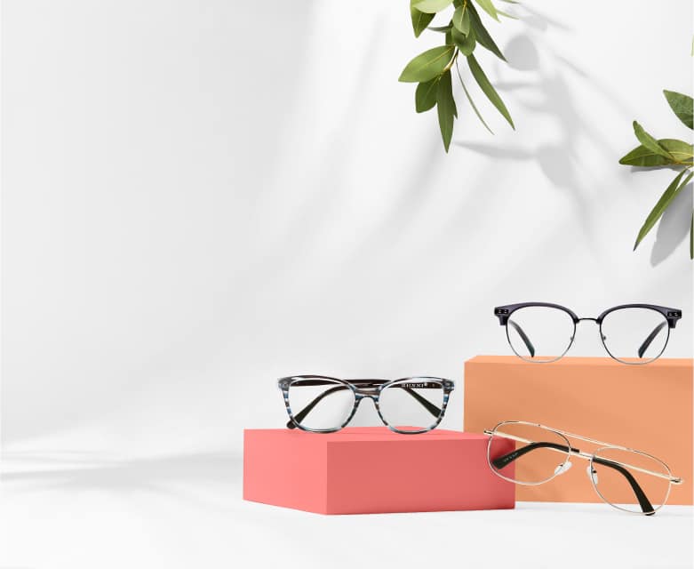 White background and orange risers with 3 prescription glasses under $30: dark grey browline glasses, blue and gray striped rectangle glasses, and gold aviators.