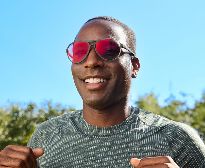 Smiling man running outside wearing Zunnies Active Style glasses with EyeQLenz with Zenni ID Guard pink-tinted lenses under bright blue sky.