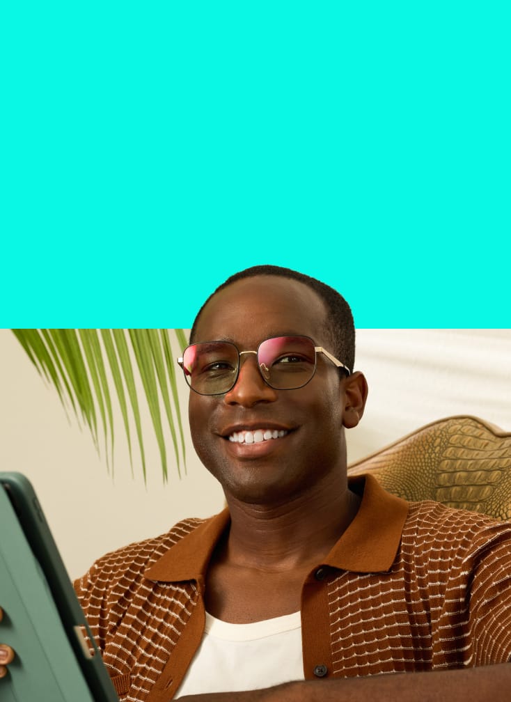 Man wearing EyeQLenz with Zenni ID Guard glasses with pink sheen, smiling while seated indoors.