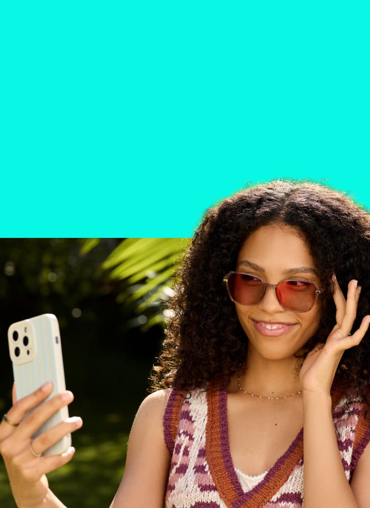 Smiling woman taking a selfie outdoors in pink-tinted EyeQLenz with Zenni ID Guard light-adaptive glasses.
