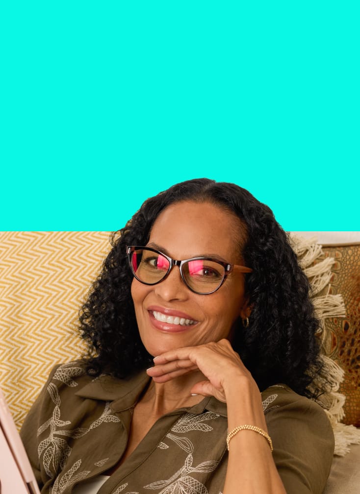 Woman relaxing and smiling in EyeQLenz with Zenni ID Guard glasses with pink-tint lenses, holding a tablet.