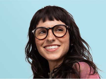 A blond woman wearing clear green glasses and a pink knit hat being hugged by a brunette woman wearing clear pink glasses and a green knit, on a light blue background with a foliage motif.