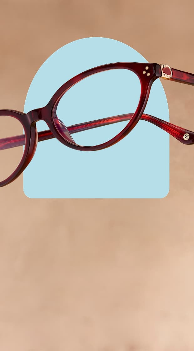 Deep red translucent oval eyeglasses with gold hinge details floating over a light blue graphic shape against a warm beige textured background.