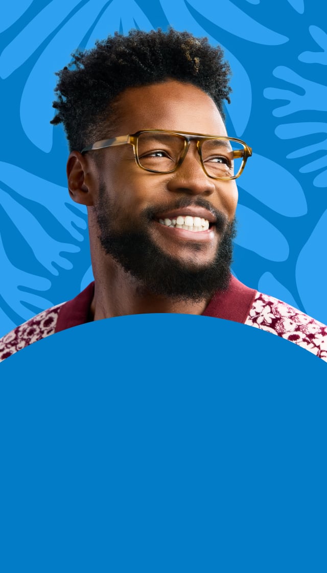 A smiling man in clear brown glasses and a patterned shirt stands before a blue background with botanical shapes.