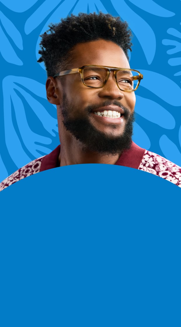 A smiling man in clear brown glasses and a patterned shirt stands before a blue background with botanical shapes.