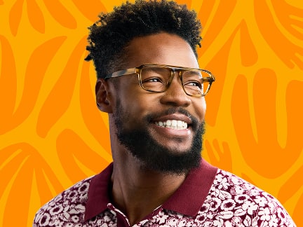Smiling man wearing tortoiseshell eyeglasses and a patterned red cardigan, standing in front of a orange background with abstract shapes.