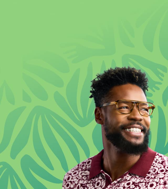 A man in tortoiseshell aviator glasses and a red patterned shirt stands before a green background with botanical shapes.