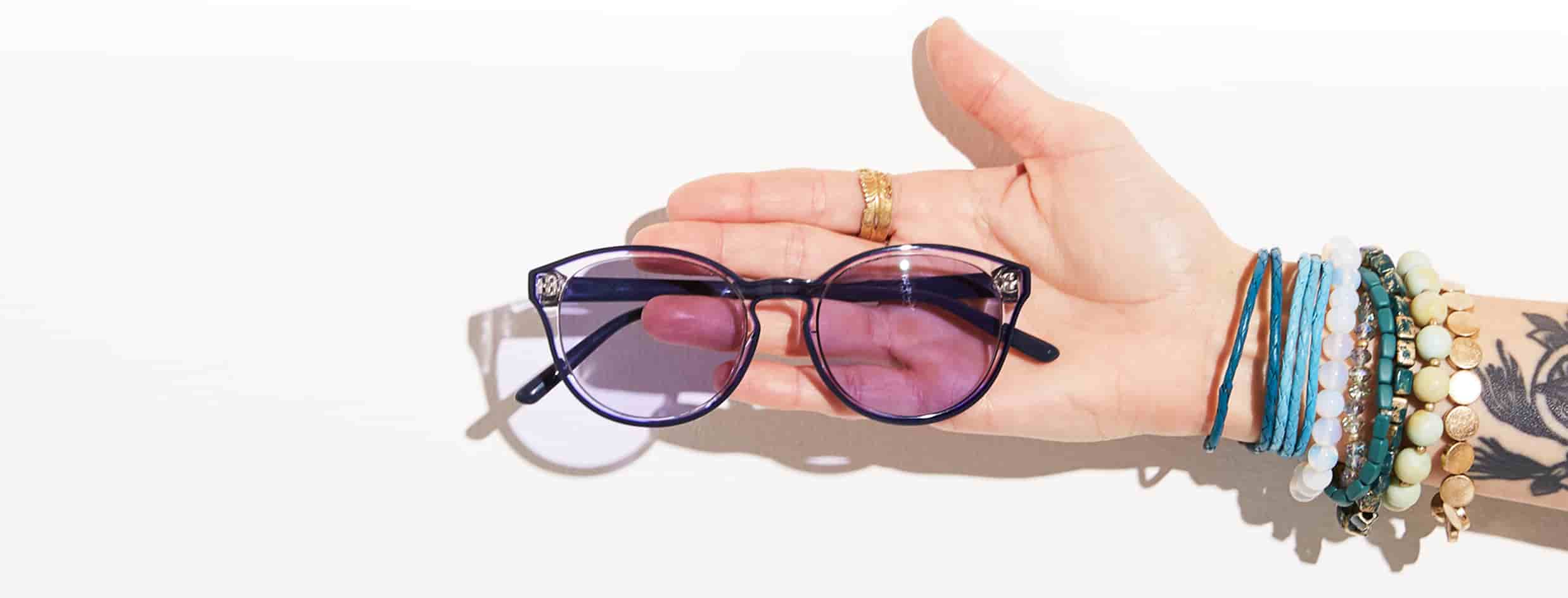 Woman’s arm adorned with bracelets and tattoo sticks out with translucent glasses #4431117 with purple tint laying on open palm.