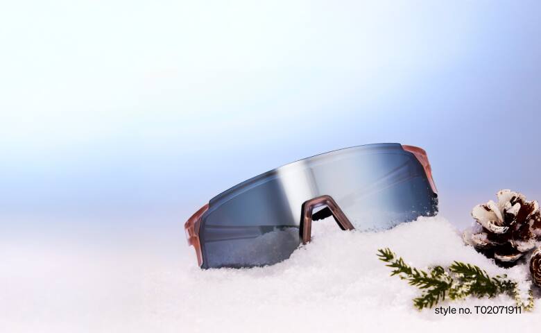 Zenni sport sunglasses with mirrored lenses on top of snow mound next to a pine cone and evergreen sprig.