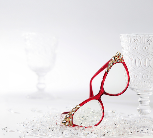 Zenni Red-framed cat-eye glasses with decorative crystals resting on a frosty white surface beside a crystal glass.