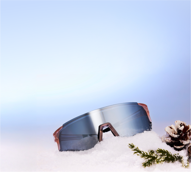 Zenni sport sunglasses with mirrored lenses on top of snow mound next to a pine cone and evergreen sprig.