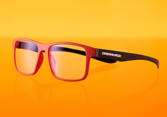 Red-framed Zenni x DreamHack glasses with clear lenses and black arms featuring 'DreamHack' printed in white, set against an orange background.