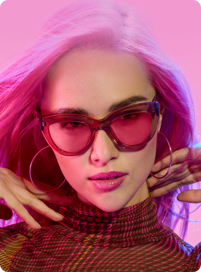 Woman wearing pink-tinted eyeglasses from the Blokz®+ Tints collection. Text reads “Colorful lenses that filter 26x more blue light than standard lenses” with a “Shop now” button.