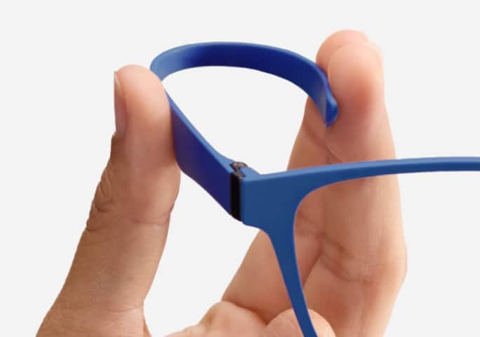 Close-up blue Zenni OptiFlex frames held between fingers, flexing the frame temple, highlighting its design on a white background.
