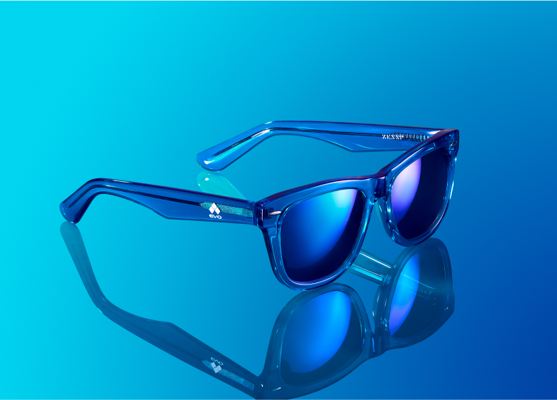 Pair of blue-framed sunglasses with reflective blue lenses displayed on a light blue gradient background. The sunglasses are positioned in a way that highlights their sleek design and reflective quality.