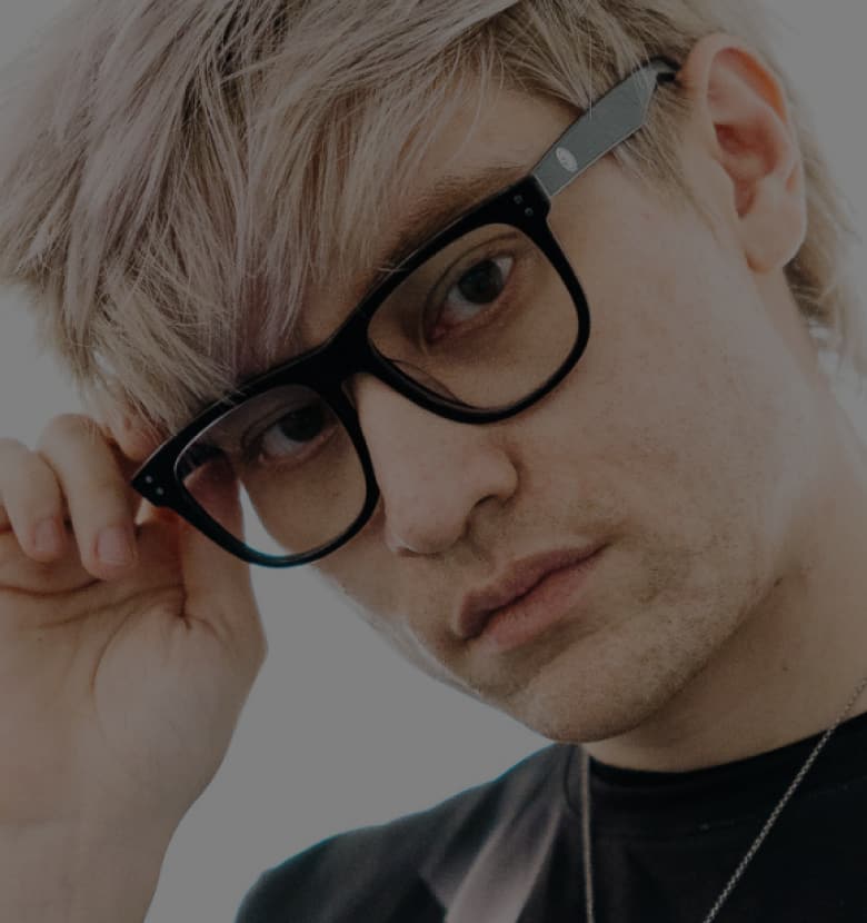 Leffen wears black-framed Zenni TSM glasses, holding the frame with one hand against a white background.