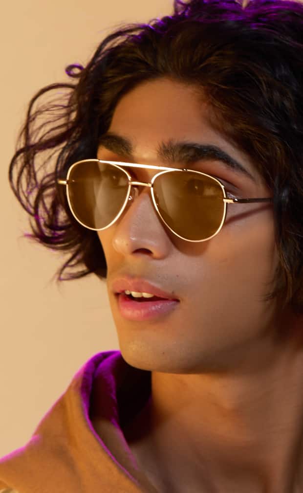 A man with short dark hair wearing metal aviator glasses with amber lenses that are reflecting magenta light.
