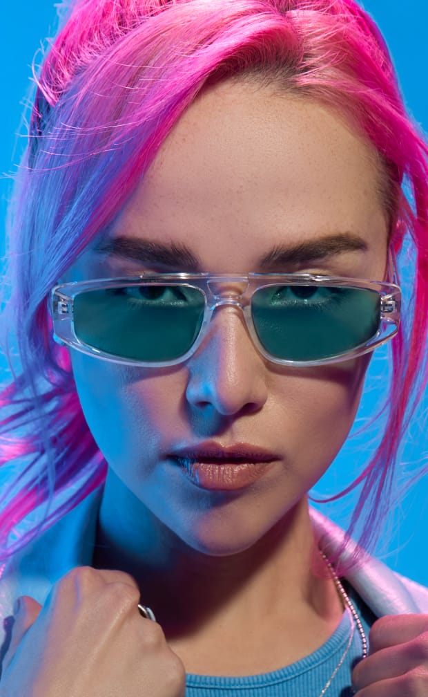 A woman with pink hair wearing plastic aviator glasses with blue lenses.