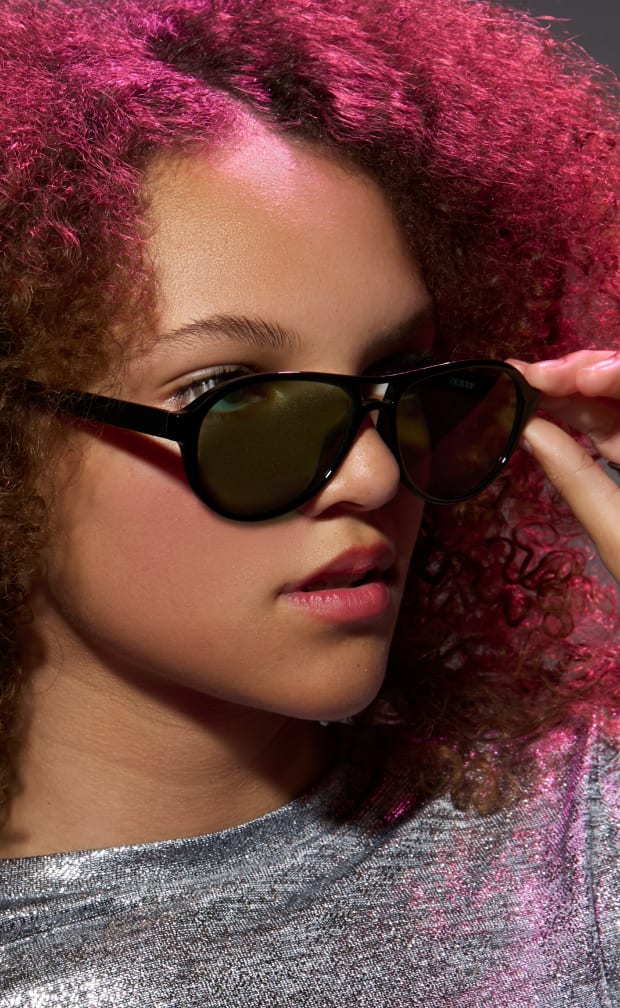 A woman with curly reddish-brown hair wearing black plastic aviator glasses with gray lenses.