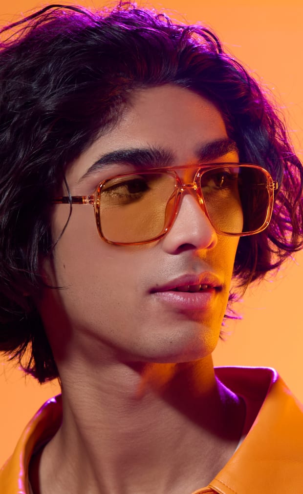 A man with short dark hair wearing orange plastic aviator glasses with orange lenses.