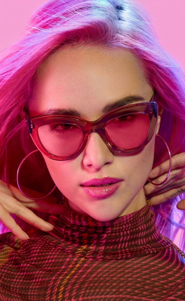 A woman with pink hair wearing light brown plastic cat-eye glasses with rose lenses.
