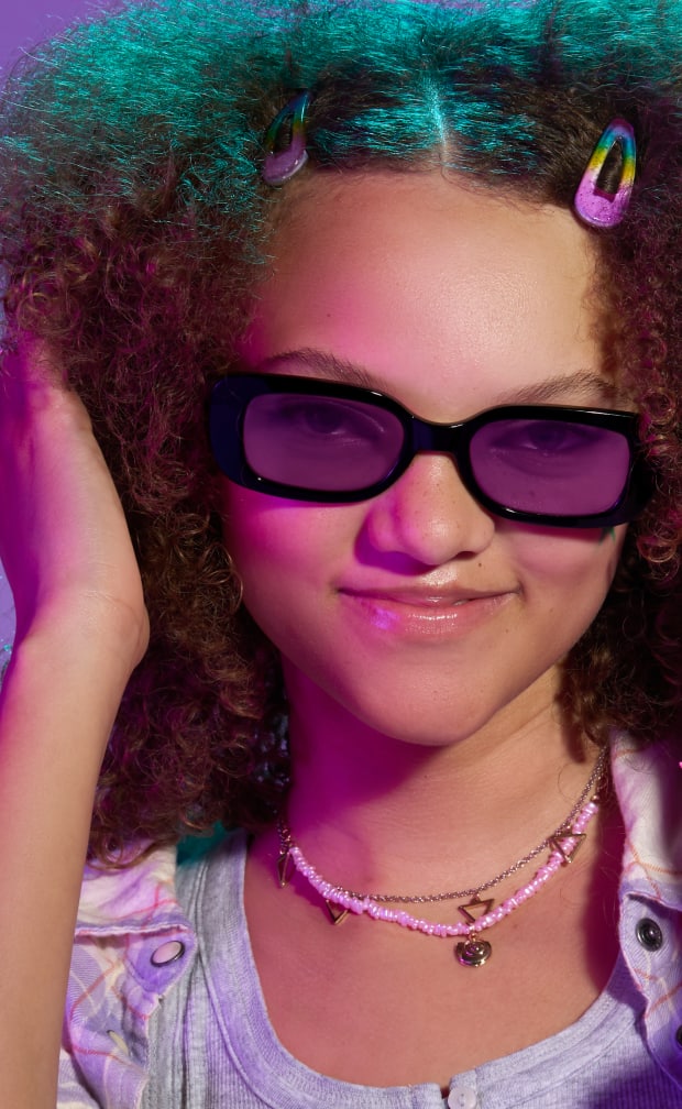 A woman with curly reddish-brown hair wearing black plastic rectangle glasses with purple lenses.