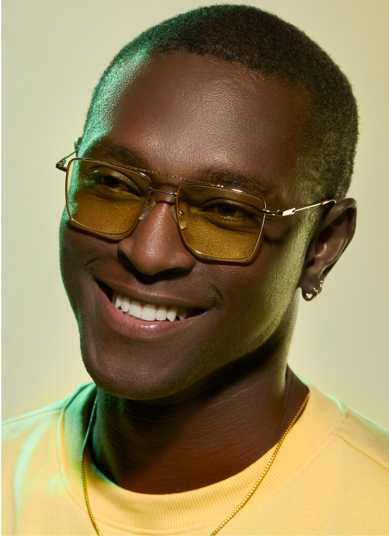 A smiling man with short buzzed hair wearing gold metal aviator glasses with yellow lenses.