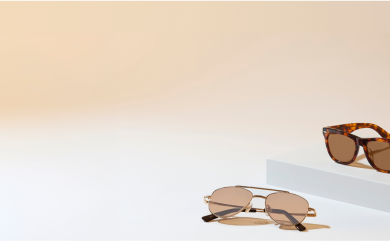 Two pairs of Zenni, one is an aviator style and one with tortoiseshell frames, both with Blokz®+ Tints amber lenses on an tan and white background.