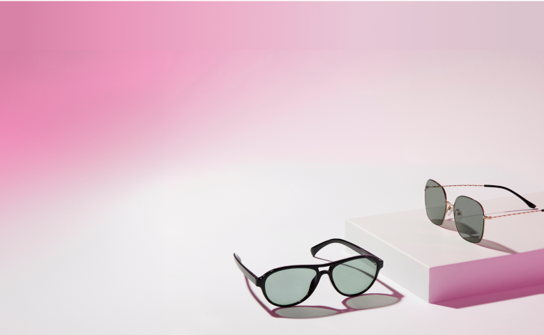 Two pairs of Zenni glasses with black frames and Blokz®+ Tints gray lenses on a pink and white background.