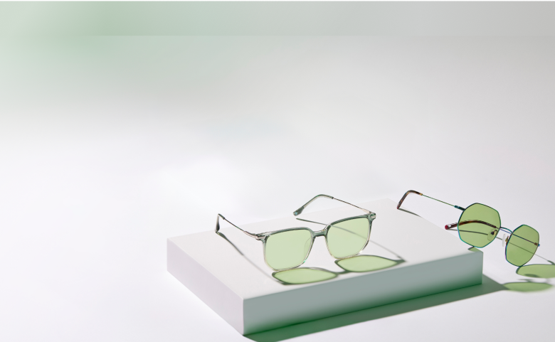 Two pairs of Zenni glasses with metal frames and Blokz®+ Tints green lenses on a green and white background.