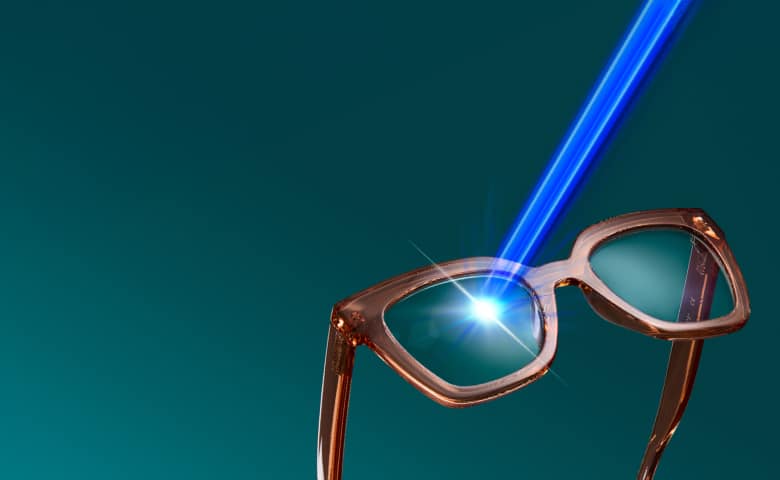 Zenni Blokz® blue light blocking glasses with brown frames on a teal background and a blue light beam being filtered through the lens. Text lists product features including 16x more blue light filtering, 100% UV protection, anti-reflective, and anti-scratch properties.