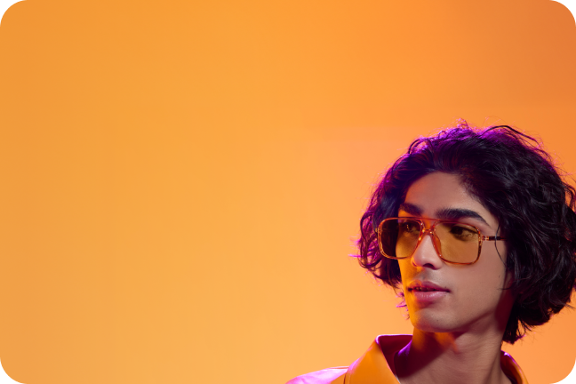 A man with curly hair wearing brown plastic aviators with yellow Blokz+ Tints lenses.