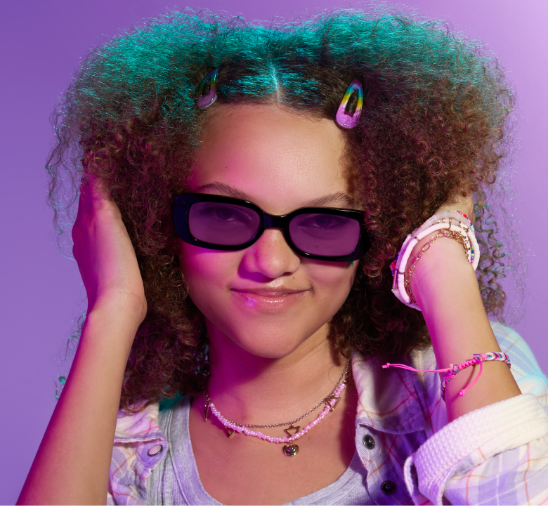 A girl with curly reddish brown hair wearing black plastic rectangle glasses with purple Blokz+ Tints lenses.