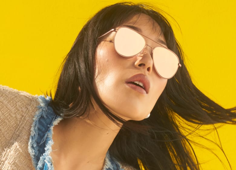 Close-up of a person wearing reflective aviator sunglasses on a bright yellow background. The person's face is partially covered by the sunglasses, and their hair flows naturally.