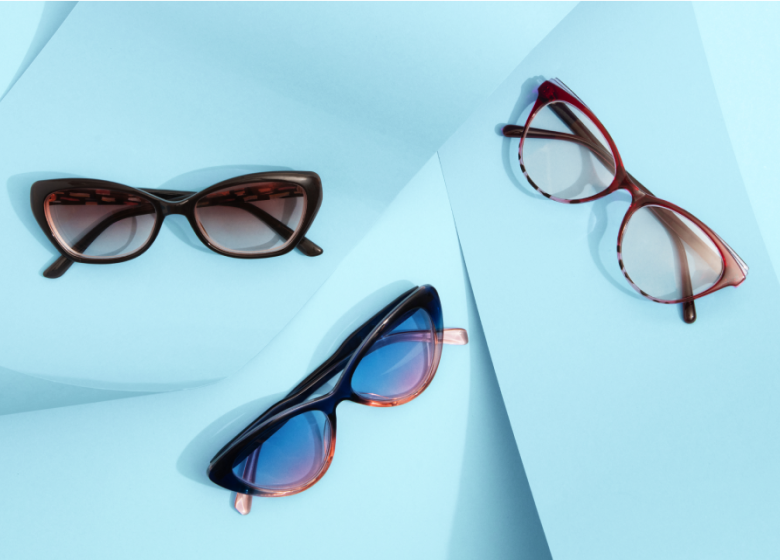 Three pairs of readers on a light blue background. Top-left: tortoiseshell cat-eye sunglasses, bottom-center: dark-rimmed sunglasses with blue-tinted lenses, and top-right: brown-rimmed sunglasses with an arrow pointing towards them.