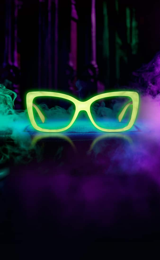 The image features a pair of neon green, cat-eye style glasses glowing against a dark background. Surrounding the glasses are swirling clouds of green and purple smoke, creating a mysterious and ethereal atmosphere.