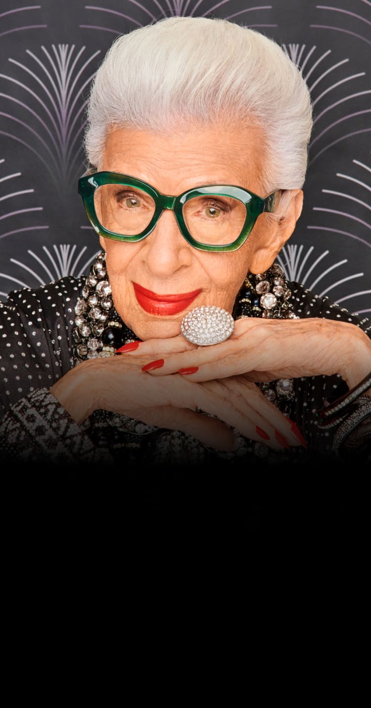 Iris Apfel wearing green-framed Zenni glasses with a black patterned background. Text: Honoring Iris Apfel (1921-2024).