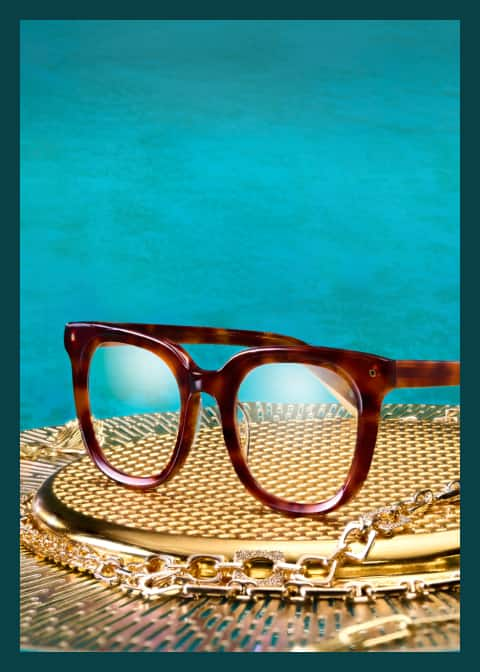 Tortoiseshell Zenni glasses from the Iris Apfel collection sit on a gold tray with a turquoise background.