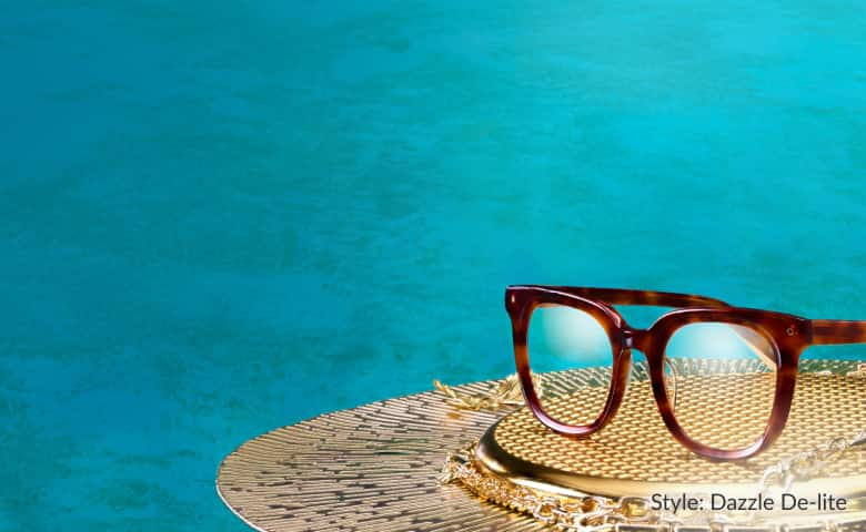 Tortoiseshell Zenni glasses from the Iris Apfel collection sit on a gold tray with a turquoise background.