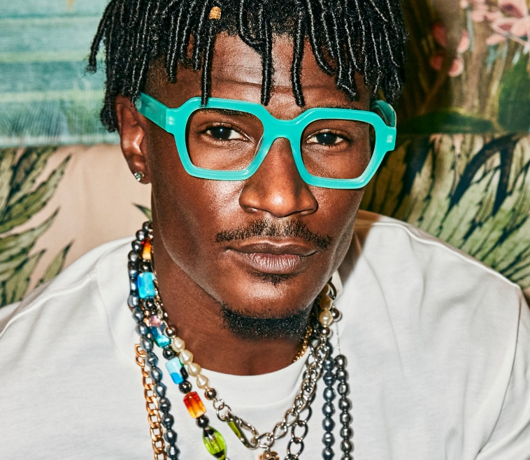 A Black young man on holiday rocking bright blue square glasses.
